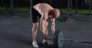 Sporcu adam spor salonunda halterdeki tabakları hazırlıyor. Güçlü sporcu ağırlık kaldırma antrenmanına hazır ol. Erkek sporcu spor malzemelerini egzersiz için hazırlıyor