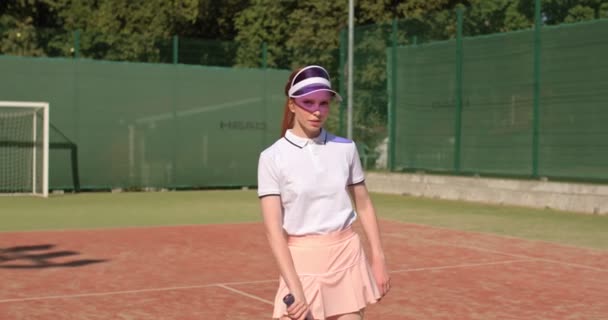 快乐的女子网球教练在网球场上的摄像机前摆姿势 迷人的姑娘抬起胳膊 闭上她的脸 阳光下的眼睛 自由自在地休息着 — 图库视频影像