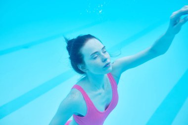 Zencefilli kız pembe mayosu suyun altında yüzmekten zevk alıyor, zevk alıyor, keyif alıyor, rahatlıyor, sporcu kadın dinleniyor, havuzda dinleniyor, kolunu kaldırmış kız yüzmeyi, dalmayı öğreniyor, yan bakış açısını kapatıyor.