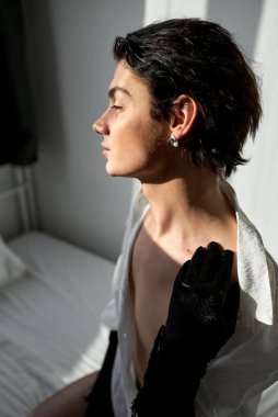 Yatakta oturan genç, seksi gay, kameraya çıplak poz veriyor. Yan görünüm portresini kapat. cinsellik