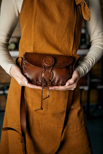 craftswoman holding orange leather bag. Close up of leather bag accessory in hand of fashion artisan leather goods foradvertisement of store or shop presentation of handmade leather product