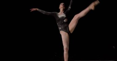 Parmak uçlarında uçlar. Genç zarif balerin tek başına un üzerinde dans ediyor, izole edilmiş siyah bir arka planda. Sanat, hareket, hareket, esneklik, ilham konsepti. Puanlı ayakkabılı klasik balerin.