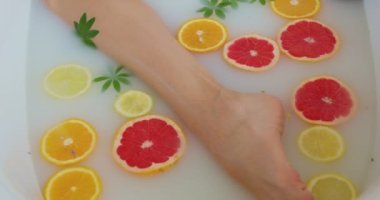 Mavi kuleyle kaplı güzel saçlı kız, yerde yatan çarşaf, süt banyosu cilt bakımı kamerasında dinlenen yavaş çekim Cleopatras Banyo 'su. Dişi, portakal ve limonla rahatlıyor. İnce bacaklar..