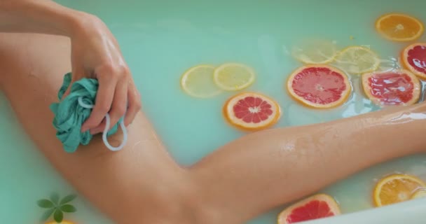 女孩用海绵按摩腿 动作缓慢 俯瞰种植的女人享用带有柑橘类水果的豪华温泉 拿着垫圈 天然的热带有机成分 牛奶橙柠檬柚子 — 图库视频影像