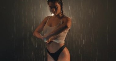 Sıska seksi kız yağmurun altında duruyor, geceleri ıslak beyaz bluzunu sıkıyor, ağır çekimde.