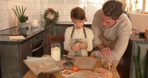 子供の男の子を持つハンサムな大人の男 クリスマスのお祝いのためのベーキングクッキーを準備する料理 家族のための自家製クッキー エプロンの十代の男の子は料理を焼くことを学ぶテーブルの後ろに立つ 幸せな瞬間 — ストック動画