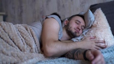 Kafkasyalı homoseksüel aile uyumadan önce yatakta. Tüylü yakışıklı adam iyi geceler öpücüğü veriyor. Uykulu erkek partneri, yatakta yatıyor.