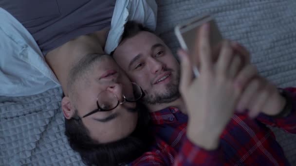 陽気男性カップルの非伝統的な向きのカジュアルな服を身に着けていますセルフィー 笑顔と携帯電話の画面を見て 同性愛と愛情の概念 — ストック動画