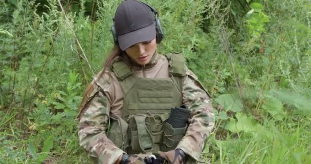 負傷した女性兵士は自分自身を助け痛みを伴う腕にトルコを適用し ペイントボールスポーツの怪我 草の上の激しい戦闘戦争からの軍事訓練 肩の痛みや事故を抱えている女性は — ストック動画