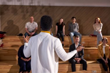 Siyah Erkek Öğretmenler Profesörünün Yetişkin Öğrencilere Taraflı Bakış Dersini Vermesi Üzerine Arka Bakış. Beyaz elbiseli yakışıklı adam bir grup insana konuşma yaparken el kol hareketi yapıyor.