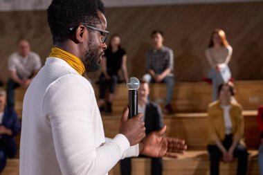 Afrikalı öğretim görevlisi, Kafkas grubuna mikrofonla ders veriyor. Genç siyahi öğretmen konferans salonunda finans hakkında konuşuyor. Gözlüklü ve beyaz giysili yakışıklıya yan bakış
