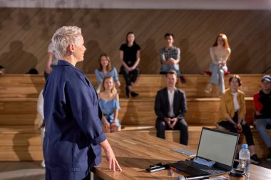 Bayan Üniversite Profesörü, Etnik Öğrencilerle dolu sınıfa ders veriyor. Seçkin Öğretim Üyesi Parlak Gençlere Öğretiyor. Yan Görünüm, Resmi Giyimde Kısa Saçlı Kadın Sözcüsüne Odaklan