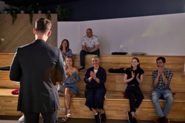 Bir grup memnun insan konferansı dinledikten sonra el çırpıyor. Resmi siyah takım elbiseli başarılı beyaz erkek konuşmacının arka görüşü. İş ve Girişimcilik. Boşluğu Kopyala