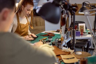 Ciddi bir kadın eski deri cüzdan işyerini restore ediyor. Resmi kapat, ön plan bulanıklaşsın