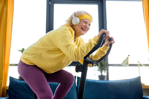 elderly caucasian female training and doing exercise on cycle at home. active pensioner lifestyle concept. Retired person training with stationary bicycle, doing workout and physical exercise