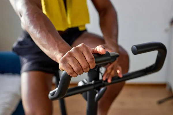 Indoor cycling, spinning cycling training. Sports training on a stationary exercise bike. cropped muscular african guy engaged in cardio workout training, shirtless male body. focus on hands