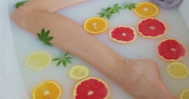 Süt banyosundaki güzel bacaklara odaklanın. Portakal dilimleriyle. Kapalı portre portresi olan seksi, şehvetli bir kadın.