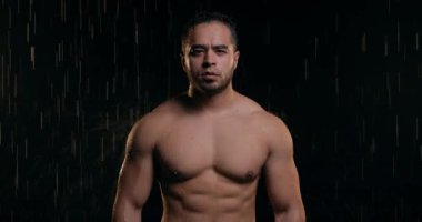 Şiddetli yağmurun altında duran yorgun, çekici, kaslı seksi adam siyah arka planda izole edilmiş. Eğitimden, antrenmandan, yorgunluktan, dinlenmeden, boş zamanlardan, yaşam tarzından sonra dinleniyor.