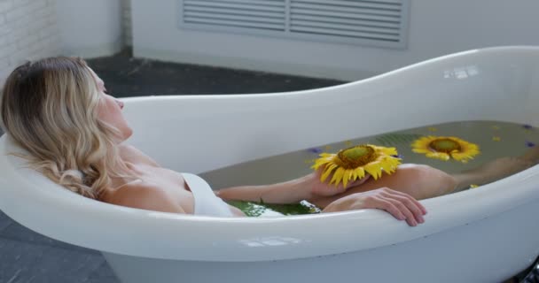 サイドビュー 目を閉じたリラックスした若い女性は 有機畑の花の遅い動きでお風呂に休んでいます 高級ホテルのフラワーバスで休んでいる熱い女の子 セクシー女性タッチ毛でお風呂に家 — ストック動画
