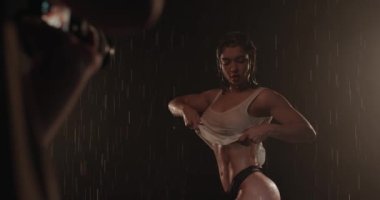 Genç, güzel esmer kadın, ıslak ve şık kıyafetler içinde poz veriyor, kameraya bakarak onları çıkarıyor..