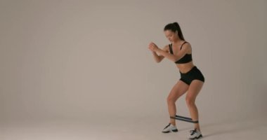 Fitness aktif bir kadının direniş bandıyla yaptığı egzersizin yan görüntüsü. İzole edilmiş gri arkaplan, kenar görüş yaşam tarzı sağlığını ve vücut bakımını görüntüledi.