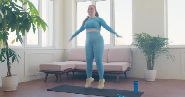快乐的微笑的女人喜欢在家里做跳跃动作 女运动员在家里做跳跃训练 胖女人高举胳膊跳 女孩做运动 — 图库视频影像
