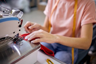 Tanımlanamayan beyaz kadın terzi modern dikiş makinesi kullanarak oturuyor. Terzi tekstil atölyesinde çalışıyor. Terzilik, küçük bir işletme ya da hobi olarak dikiş dikmek. Dikiş işlemi