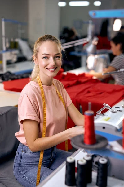 Textile cloth factory working process tailoring modern clothes, young beautiful caucasian woman at work, engaged in tailoring using modern sewing machine. dressmaker enjoy sewing,look at camera