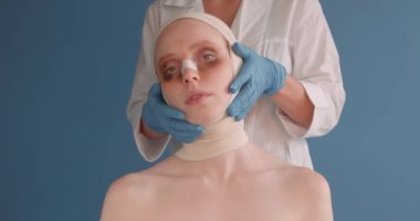 Gözlerinde morluklar olan mutsuz üzgün kız ameliyattan sonra, mavi arka plan, kadın yüzüne dokunan yavaş çekim doktorları ameliyattan sonra cilt kontrolü yapıyor.