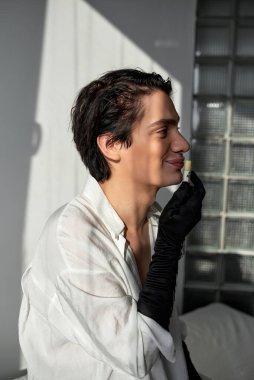 Genç adam ruj tutuyor, dudak parlatıcısı dudakları boyuyor hazırlanıyor gay makyajı, boş zaman, yaşam tarzı, yan bakış açısı