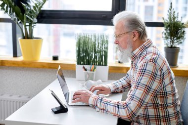 Evde otururken sosyal medyayı kontrol eden, haberleri okuyan ya da internetten alışveriş yapan yaşlı bir adam. Kendinden emin, gri saçlı, rahat bir odada oturmuş web sörfü yapıyor, çalışıyor ve çalışıyor.