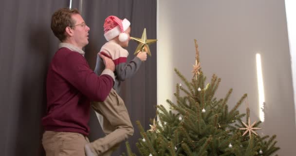 父と息子は休日の前夜に一緒にX Masツリーを飾る 家族の概念 クリスマスと新年を祝う2022 一緒に楽しく幸せな時間を持っています カジュアルウェアの大人の男と十代の男の子 — ストック動画