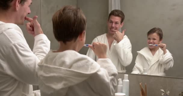 孩子和爸爸刷牙 带着牙膏和刷子的孩子牙科和口腔卫生 儿童健康的日常活动 在家里洗澡或洗澡后的小孩 爸爸穿着白色浴衣的男孩 — 图库视频影像