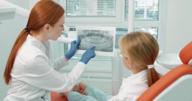 Dişçi kadın doktor sevimli genç bir hastaya çenesinin resmini gösteriyor. Sağlıklı yaşam tarzı kavramı. Ağır çekimde dişler yavaş çekimde bakım yapar
