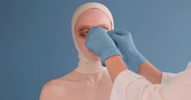 医者は事故にあった女性の鼻に胸を張って肖像画を閉じ国内暴力虐待者の犠牲者脳震盪肖像画を閉じて隔離された青の背景 — ストック動画