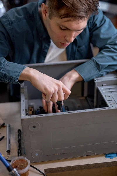 young professional repairman unscrewing screws from computer case with screwdriver for repair and maintenance. repair and maintenance of computers, pc. concentrated caucasian guy at workshop