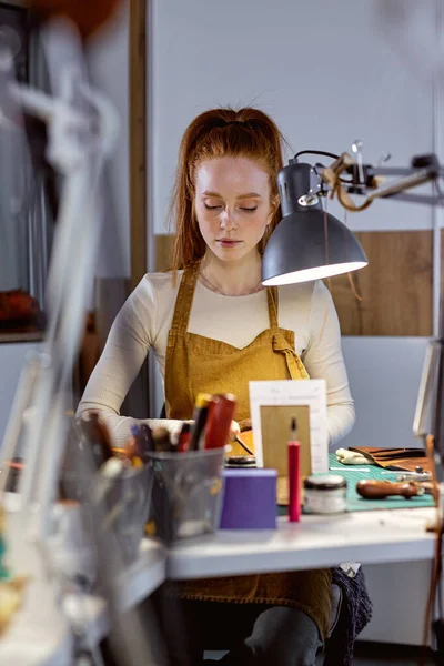 stock image young beautiful red-haired serious girl working with awl, making clothes, sewing belt, bag, purse, footwear. close up portrait.