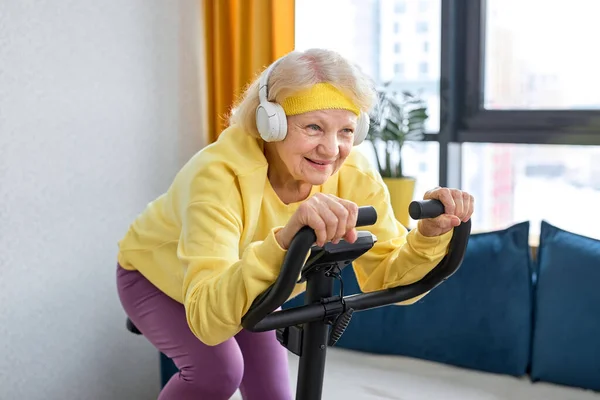 elderly caucasian woman training and doing exercise on cycle at home. healthy pensioner lifestyle concept. Retired woman training with stationary bicycle, doing workout and physical exercise