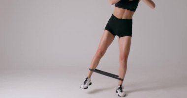 İnce beyaz kız kalça kaslarını çalıştırmak için bantlı bacak kaldırma hareketi yapıyor. Sporcu, direnç bandıyla yan bacakları kaldırıyor. Mekanın yavaş çekim çekimini taklit ediyor. Spor yapan atletik kız egzersiz yapıyor.