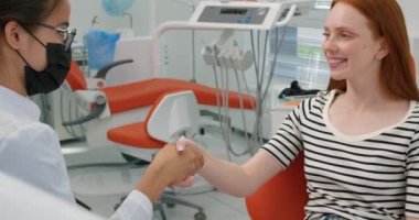 Gülümseyen mutlu kadın kızıl saçlı hasta başarılı tedavi için dişçiye gidiyor. Hasta ve doktor el sıkışıyor. Yavaş çekimde teşekkürler.