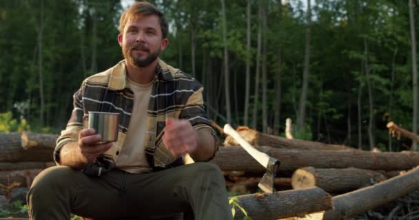幸せなハンサムなハンサムな木材ジャック労働者は 森の中に座って カップからお茶を飲みながら カメラを見て笑っている ポートレートを閉じるスローモーションフリースペアタイムライフスタイル — ストック動画