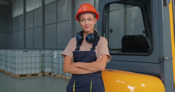 工厂物流运输仓库叉车司机旁的女工笑着摆出一副双臂 身穿制服 头戴橙色防护帽的样子 成功地做好了工作 — 图库视频影像