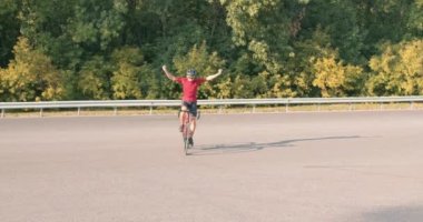 Profesyonel motorcu kollarını kaldırarak yarışı kazanmasını kutluyor. Neşeli bisiklet sporcusu, sakin kırsal alanda zaferi kutluyor. Profesyonel bisikletçi, elleri olmadan neşeli bir şekilde yol bisikleti sürüyor. eğlence mutluluğu.