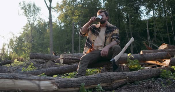疲れた汗だが陽気な男はお茶や水を飲む男はカップを持っている男は倒木や丸太の上に座って夏の夜遅い動き休憩時間 — ストック動画