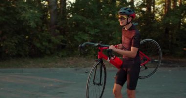 Gülümseyen mutlu aktif motosikletli adam yaz günü bisikletini açık havada taşıyor. Bisikletçi antrenmanı bitirdi, ağır çekim.