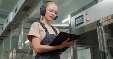 aktif hırslı kadın işçi kulaklıkla robot hattında şişeleme, şişelere, kutulara böcek ilacı paketleme, tablete not alma, kağıt üzerine kalemle yazma. üretim, imalat