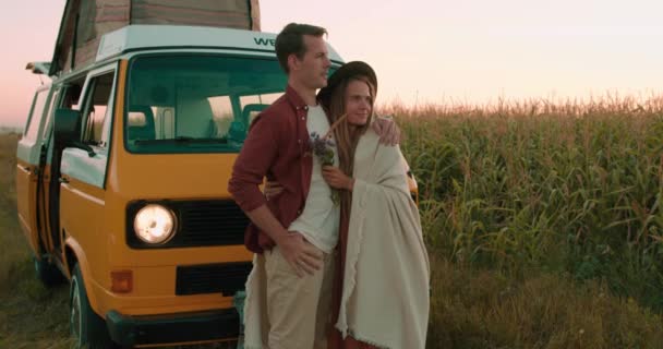 スローモーションロマンチックな若い愛情カップルトウモロコシ畑で抱擁 男は毛布に包まれた女性を受け入れます田舎で素晴らしい夕日を見て楽しんで家族 愛関係黄色のキャンパーバン — ストック動画