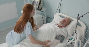 Genç mutsuz kadın, hasta babasının elini tutarak hastane yatağında ağlıyor. Stresli kız, hastane koğuşunda hasta yaşlı bir adamı ziyaret ediyor. Aile Sağlık Hizmetleri İnsan Duyguları Birimi.