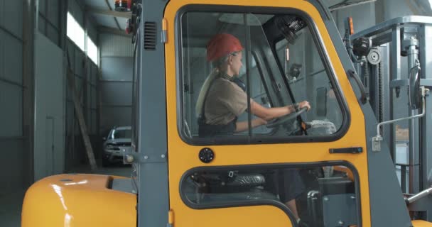 フォークリフトの女性ドライバーは棚に置くためにペシデスと容器と倉庫倉庫に乗ることになる 作業中のヘルメット駆動倉庫ローダーの従業員スローモーション — ストック動画