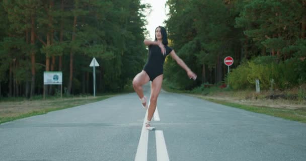 笑顔ブルネット才能バレリン女の子で黒スーツとポイントの靴は 夏の夜明けに道路上で調達足で旋回 フットターの動きを実行し スローモーション ダンサーは屋外で足を上げる — ストック動画